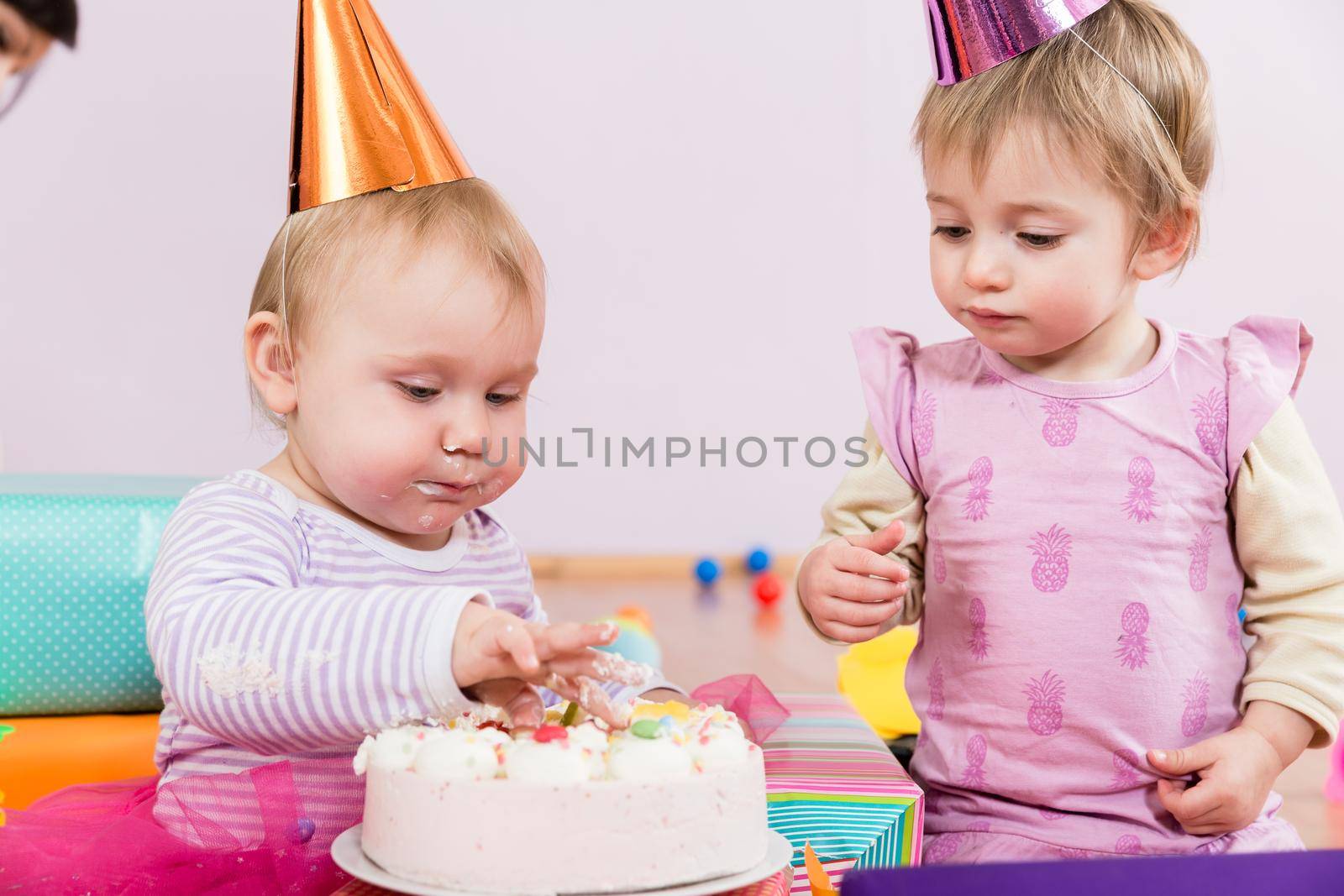 Two toddlers with party heads with birthday cake