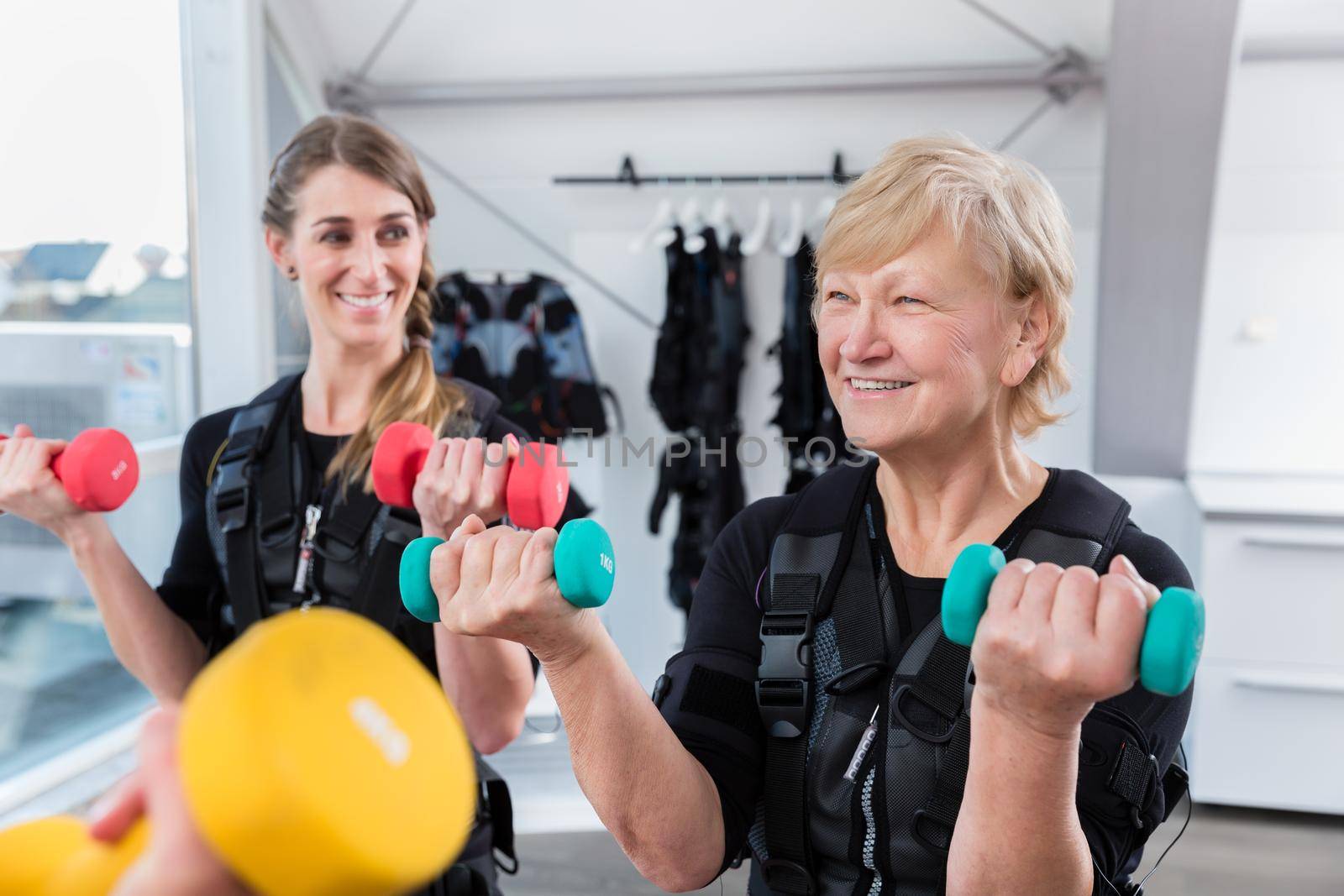 Senior and young woman during wireless ems training with weights