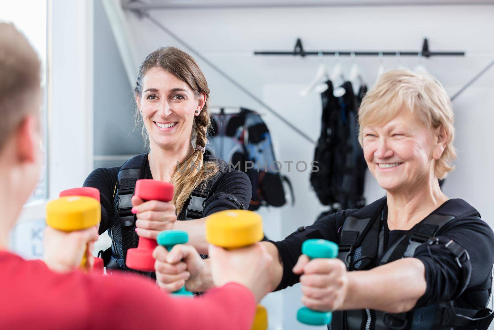Senior and young woman with dumbbells in wireless ems gym exercising their arms