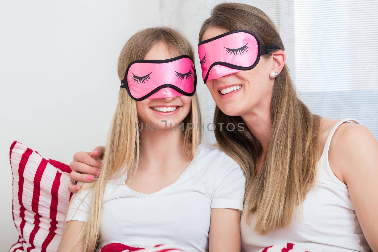 Mother and daughter wearing sleeping masks in bed by Kzenon