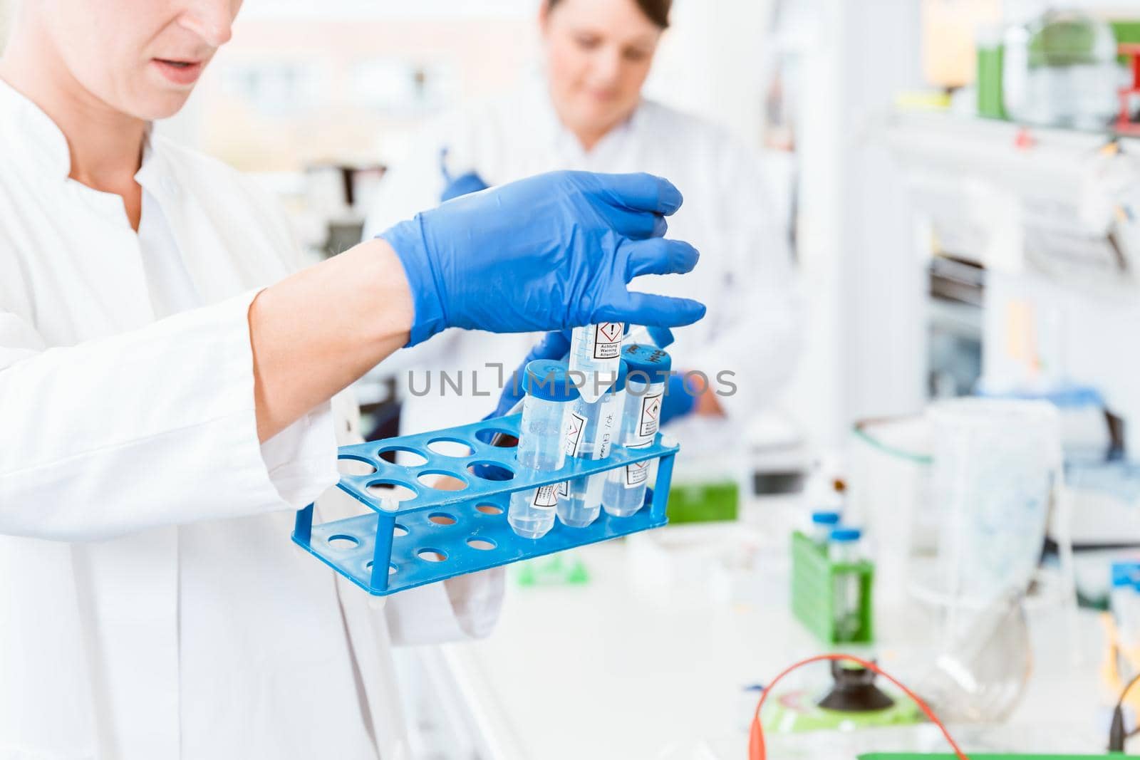 Close up of young female scientist wearing blue gloves observing tube in clinical laboratory