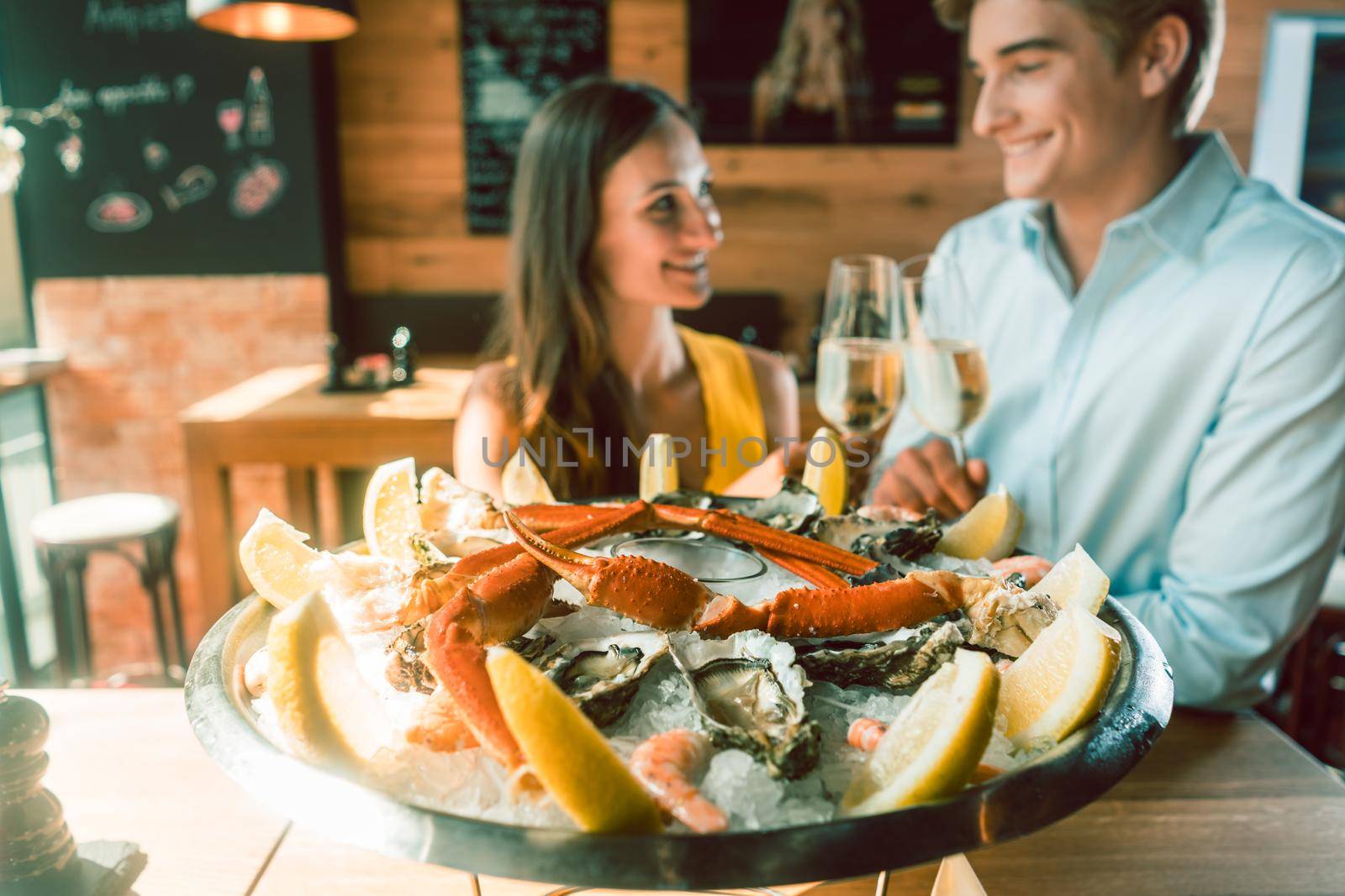 Close-up of fresh oysters and crabs served on ice with slices of lemon at the table of a romantic young couple eating at restaurant