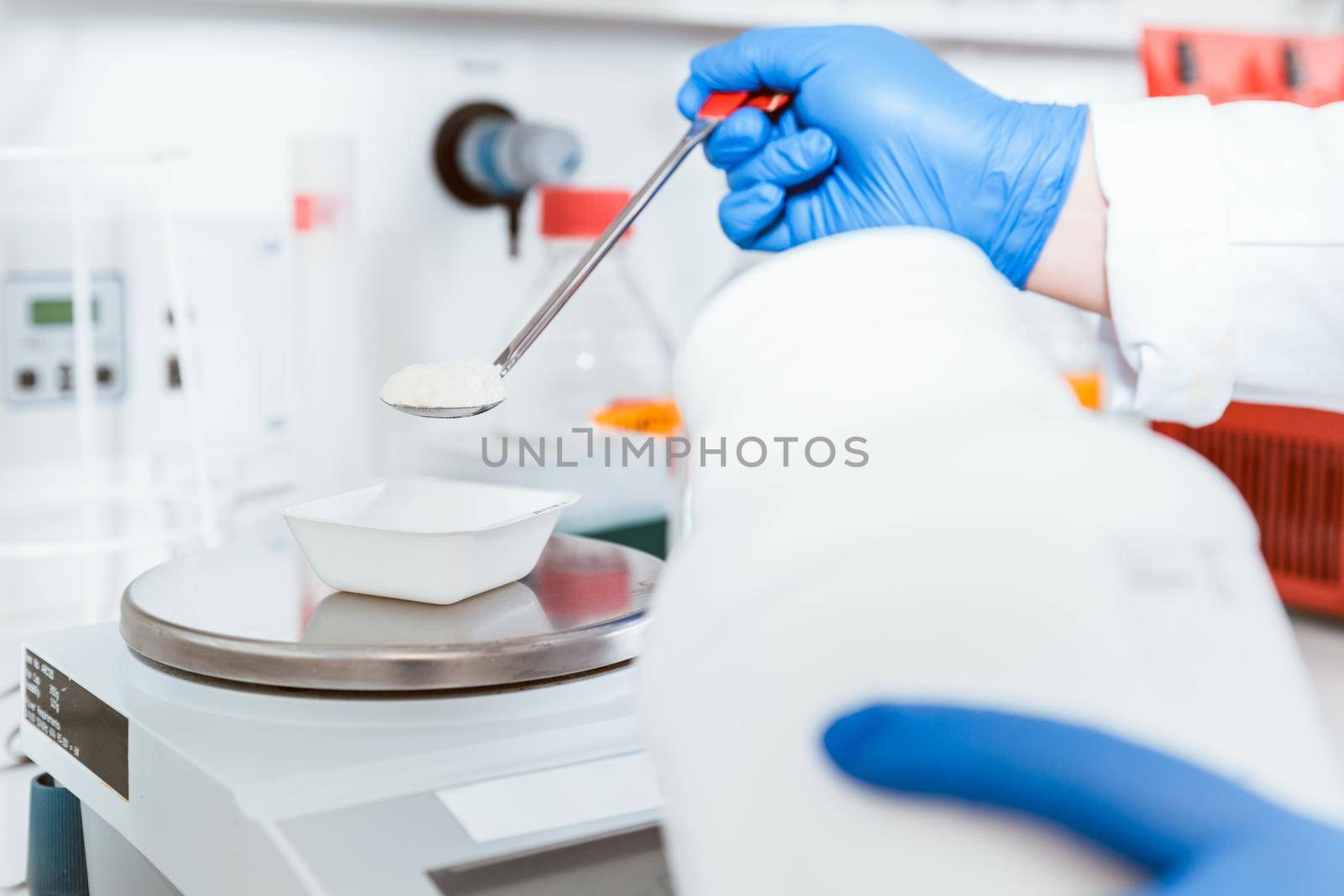 Closeup of pharmacist hand wearing blue gloves pouring white powder chemical on weighing scale in laboratory