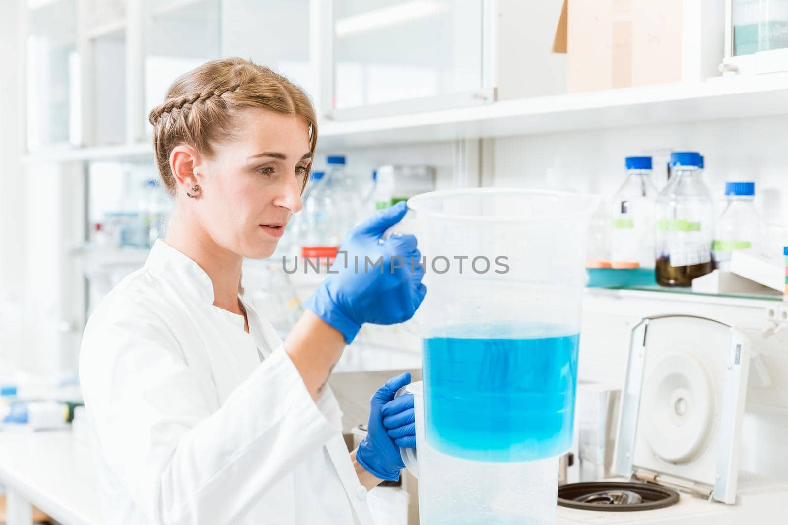 Young focused female doctor looking at blue liquid in beaker while performing experiment in laboratory