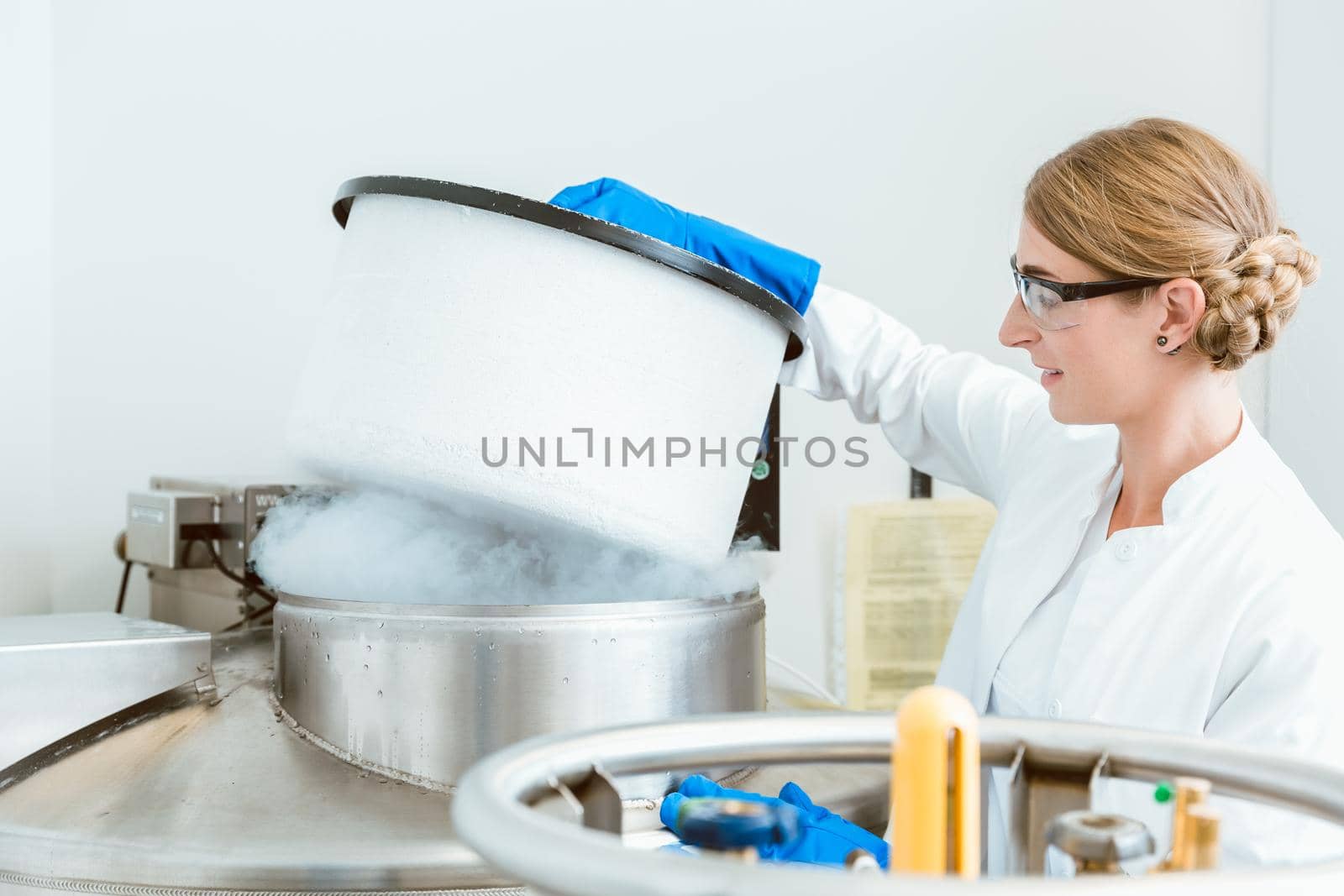 Side view of young female caucasian scientist wearing glasses lifting lid of machine in laboratory