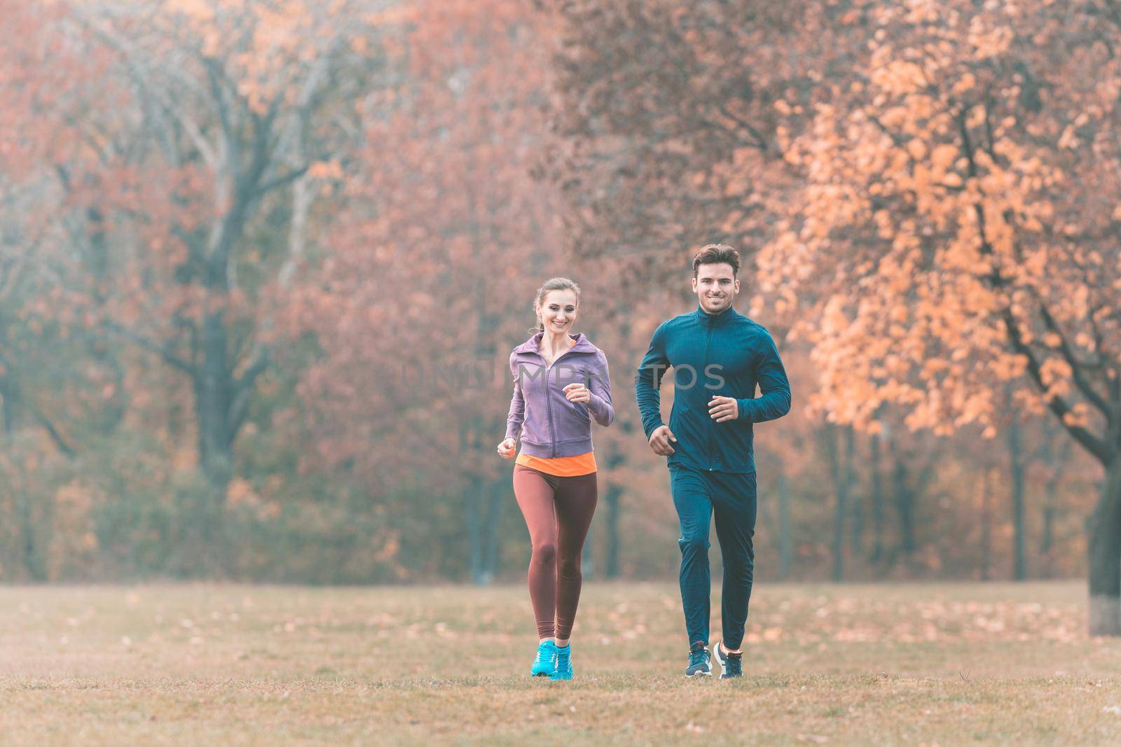 Couple in wonderful fall landscape running for better fitness towards the camera