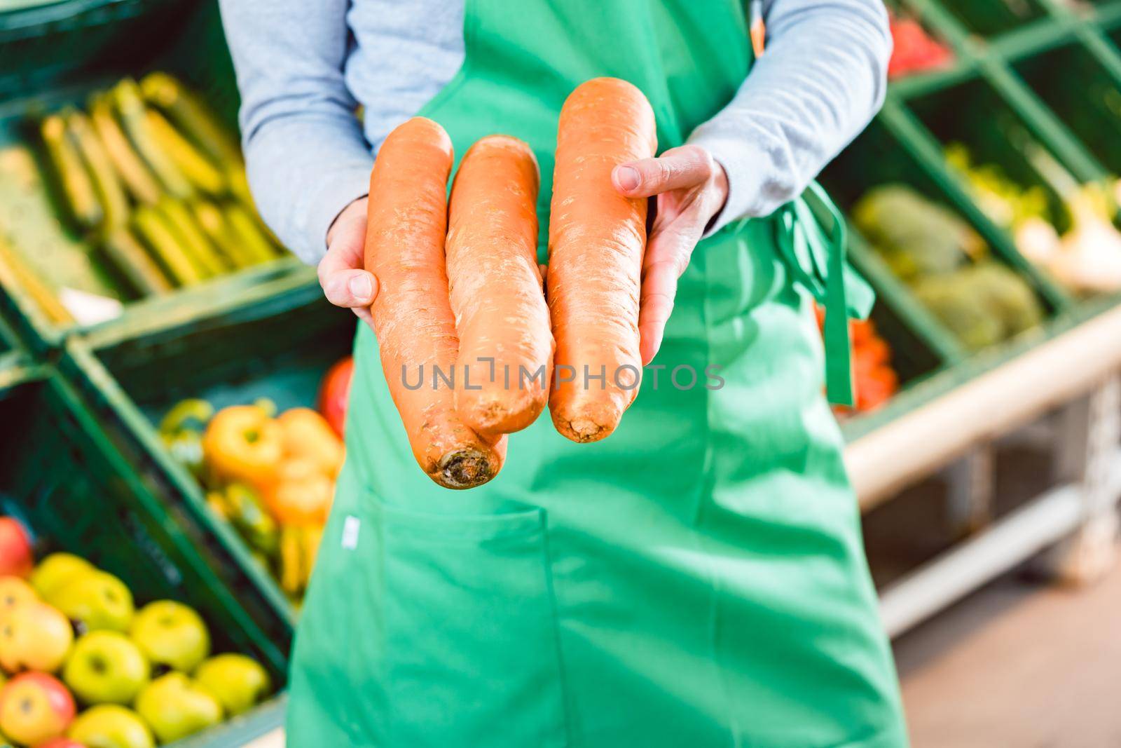 Saleswoman in organic supermarket offering fresh carrots by Kzenon