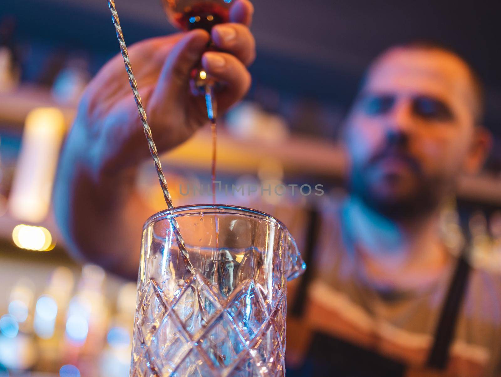 Barman pouring alcohol into empty glass to make drink in pub by Kzenon