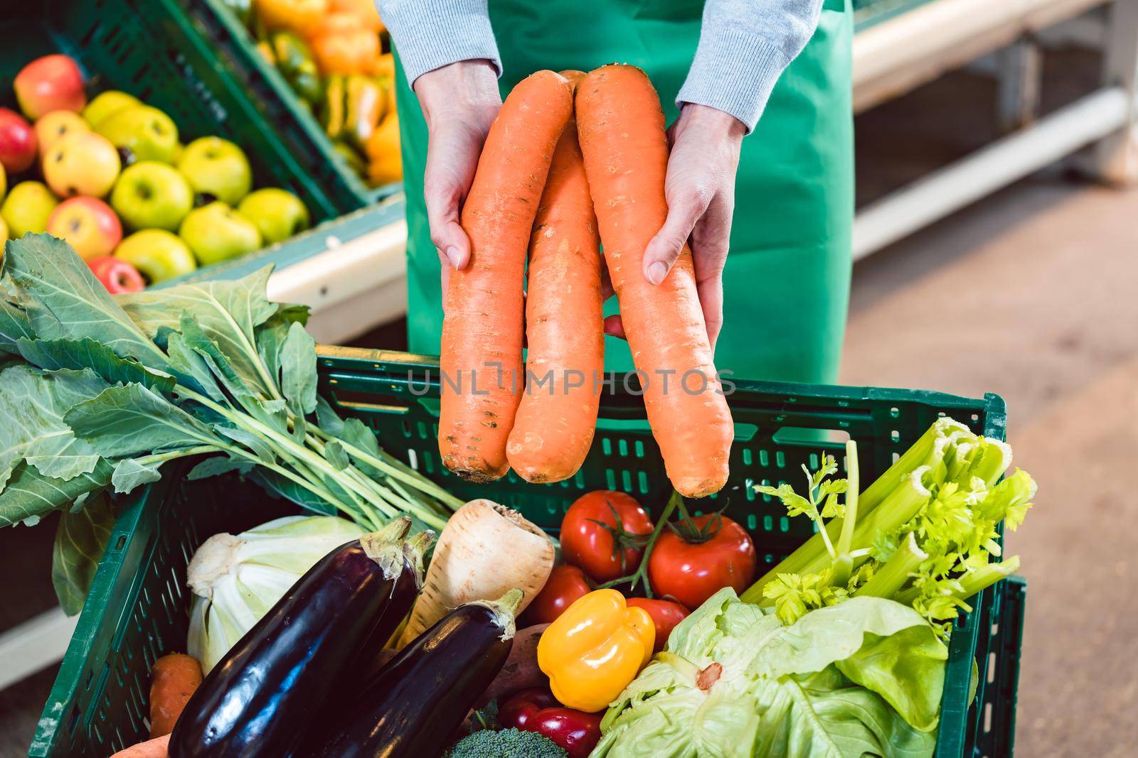 Saleswoman in organic supermarket offering fresh carrots by Kzenon