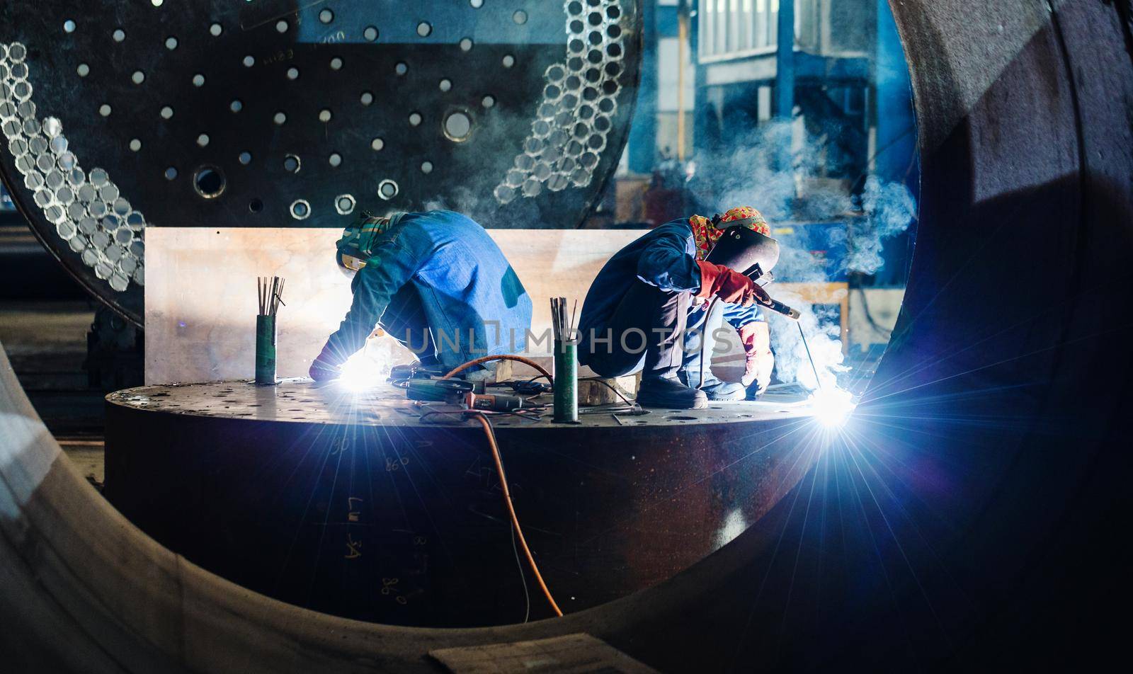Two workers welding in a factory manufacturing boilers by Kzenon