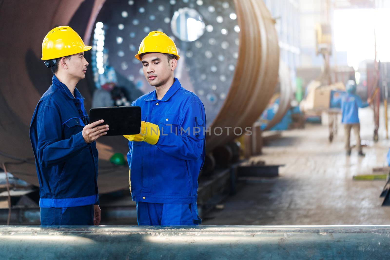 Asian experts checking information on tablet PC while supervising work in a modern factory