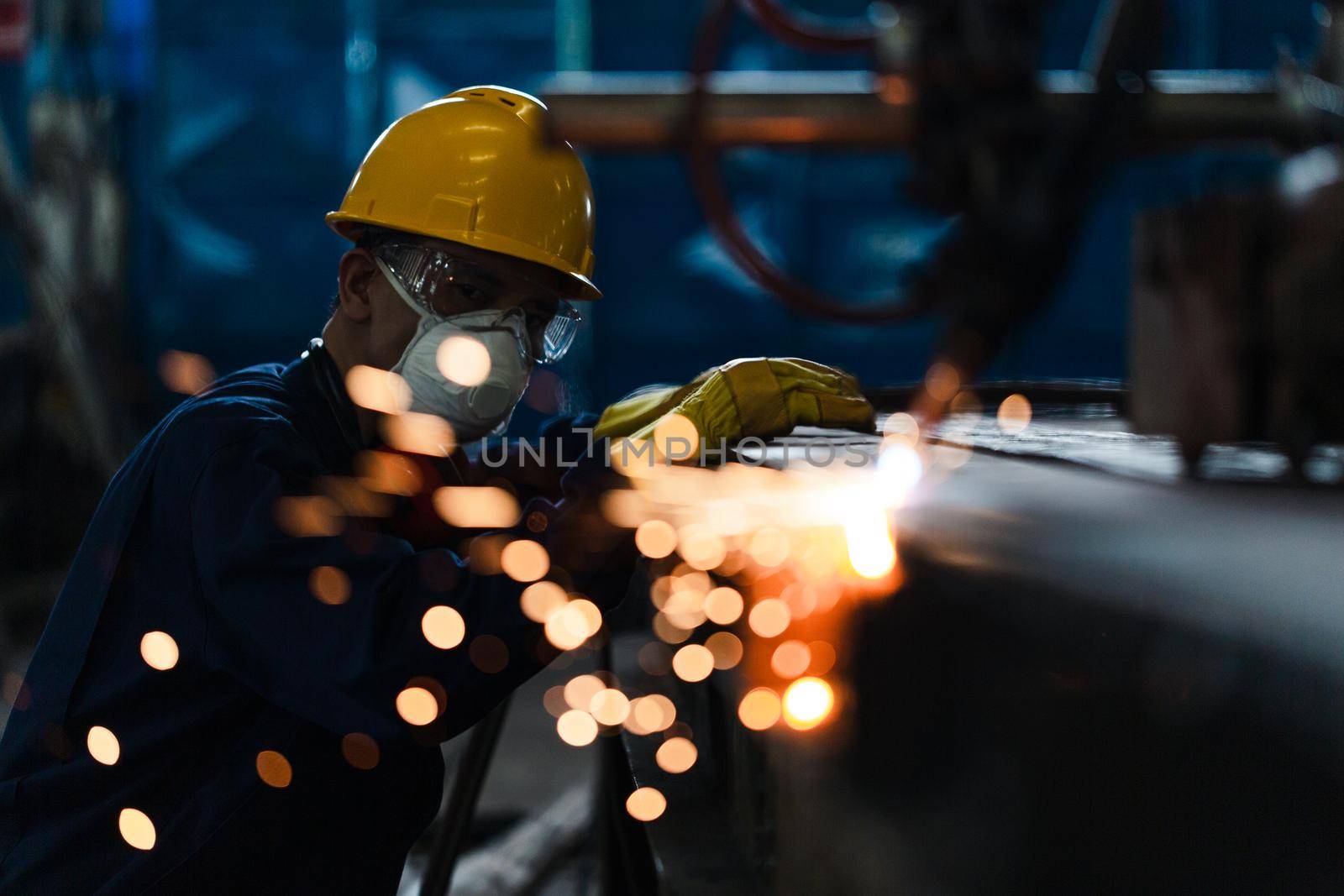 Asian worker wearing protective equipment while using CNC plasma cutter