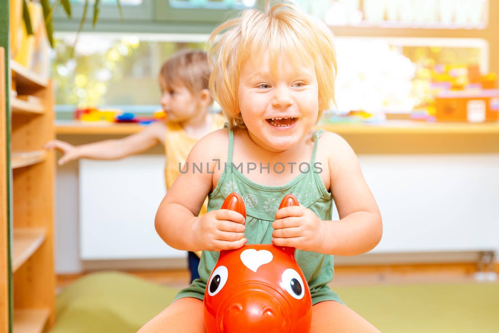Little girls riding on red and yellow play horses in kindergarten