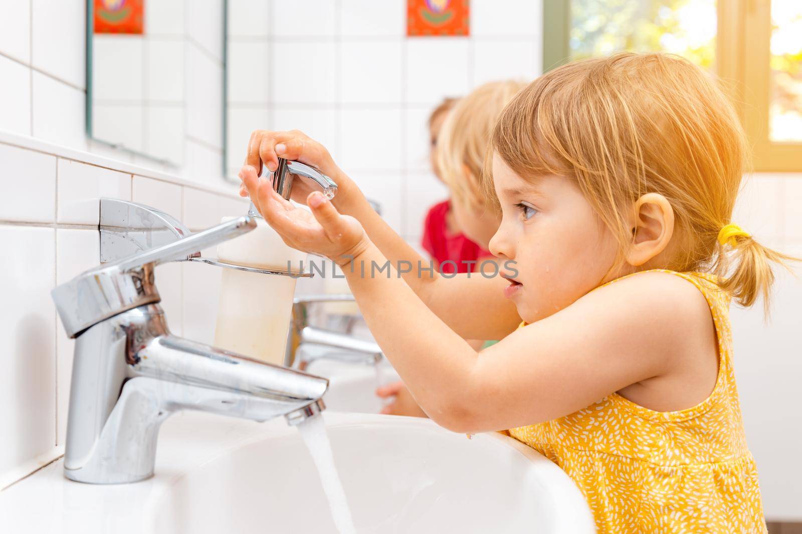 Child in kindergarten washing her hands in bathroom