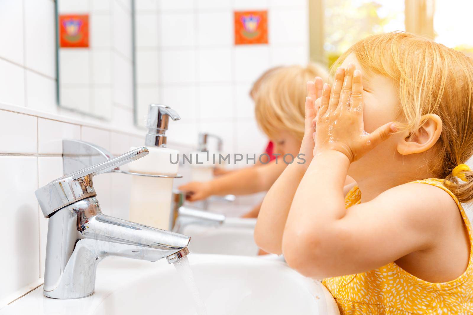 Child in kindergarten washing her hands by Kzenon