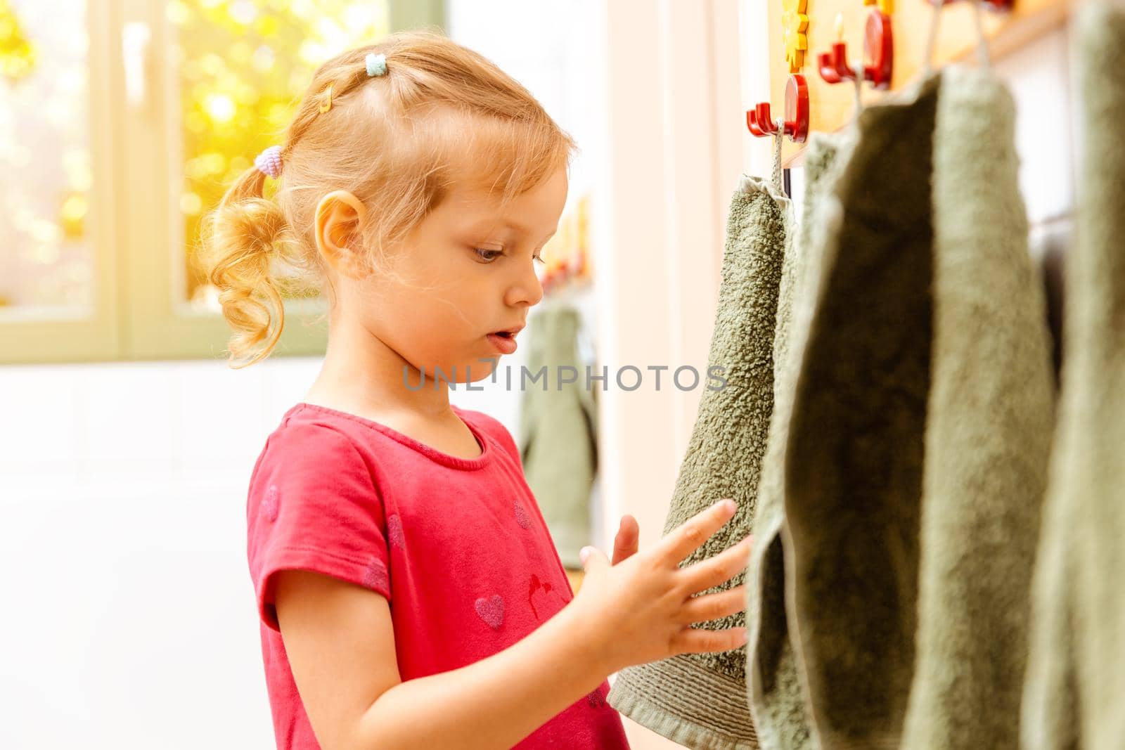 Little girl in nursery school using towel in bathroom drying her hands