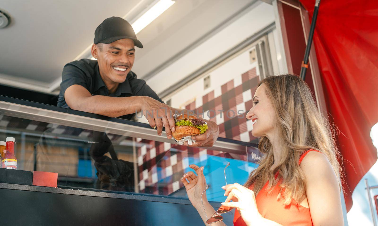 Friendly Cook in a food truck handing tasty burger over to woman customer