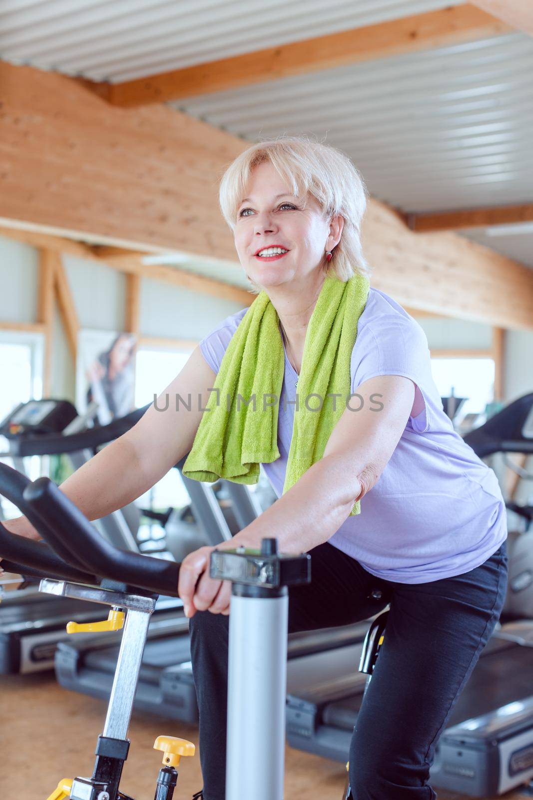 Senior woman exercising for better fitness on a bike in the gym by Kzenon