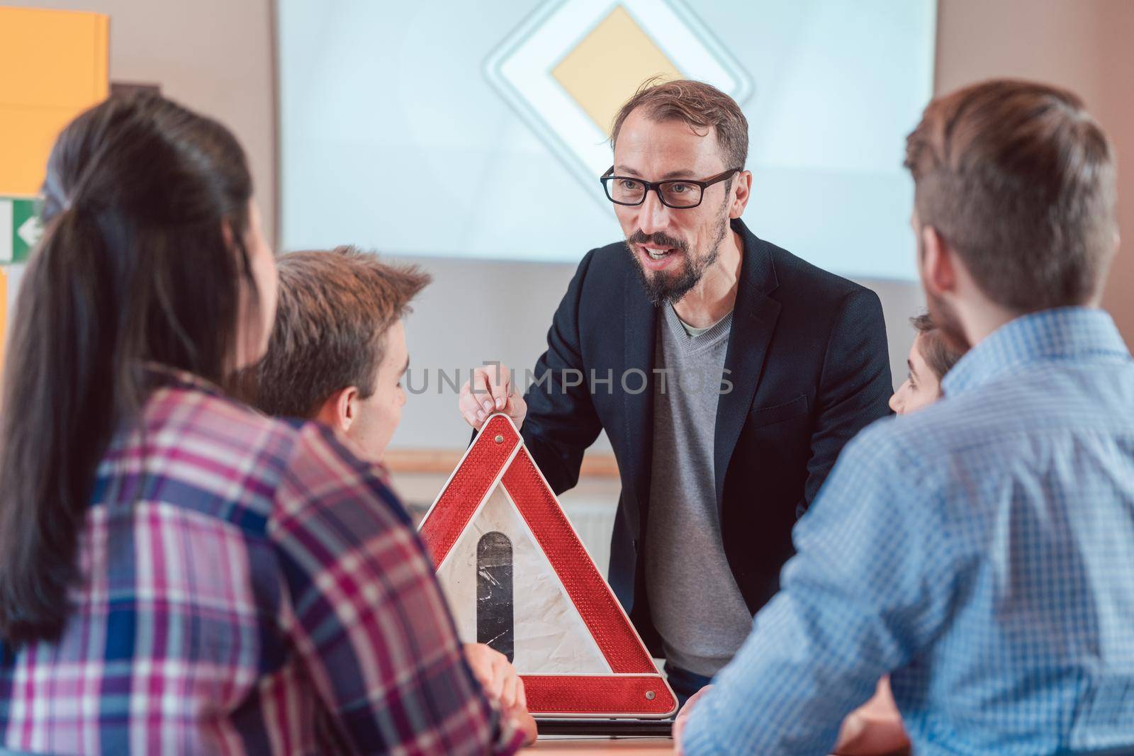Extremely competent driving instructor holding a warning triangle in class with his students