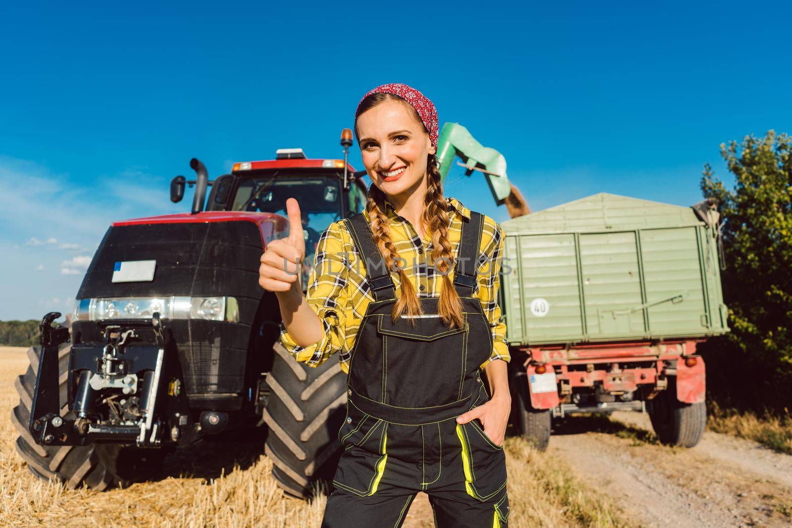 Farmer woman in front of agricultural machinery giving thumbs-up by Kzenon