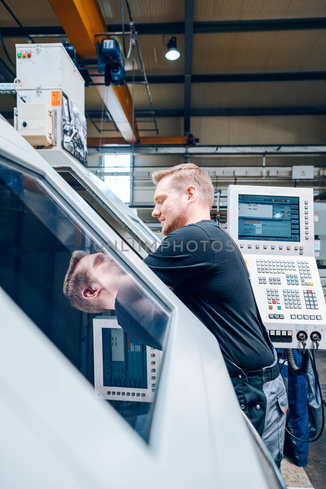 Worker resetting a cnc lathe machine in manufacturing factory by Kzenon