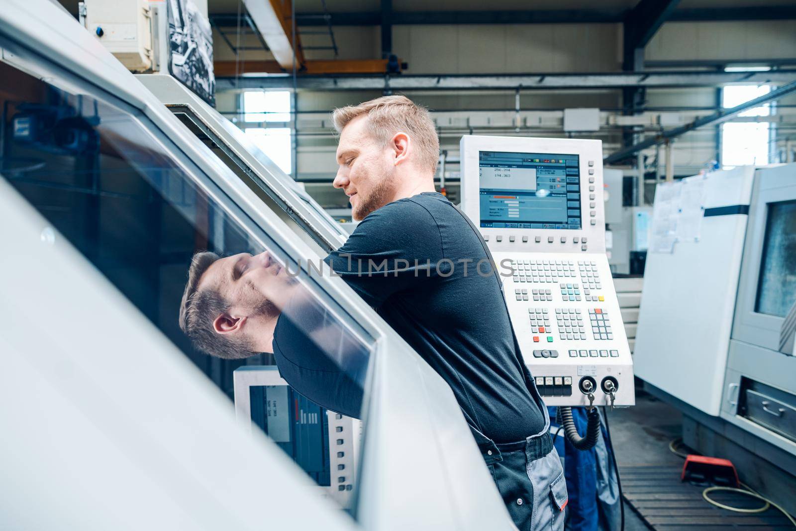 Worker resetting a cnc lathe machine in manufacturing factory by Kzenon
