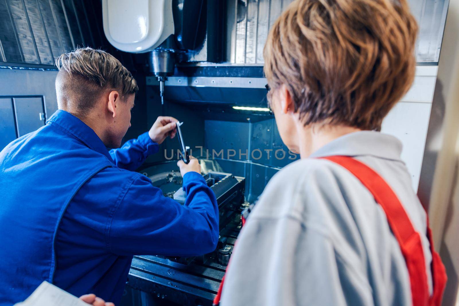 Supervisor woman watching young worker changing setup of lathe machine