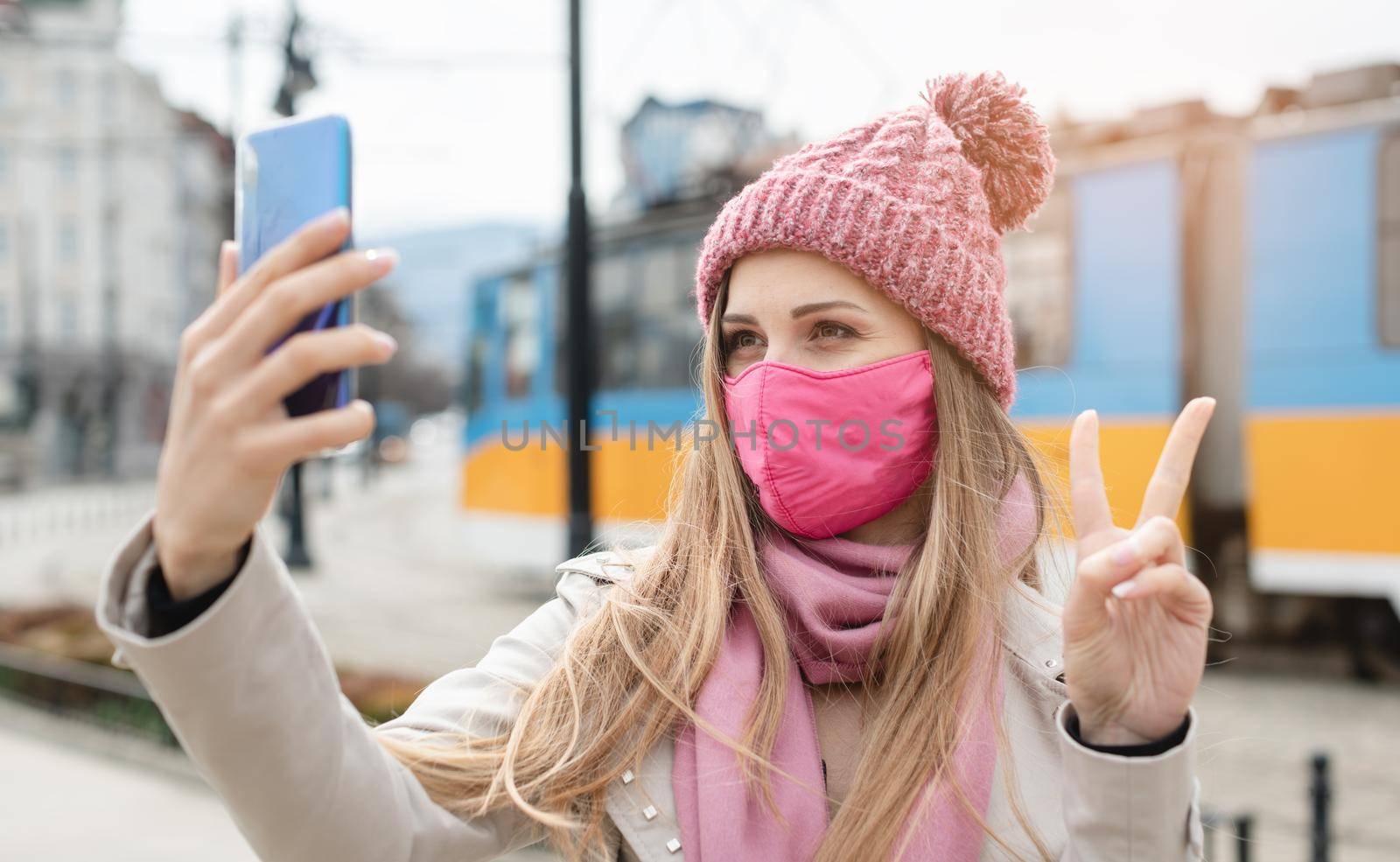 Woman doing victory sign making selfie with phone wearing mask by Kzenon
