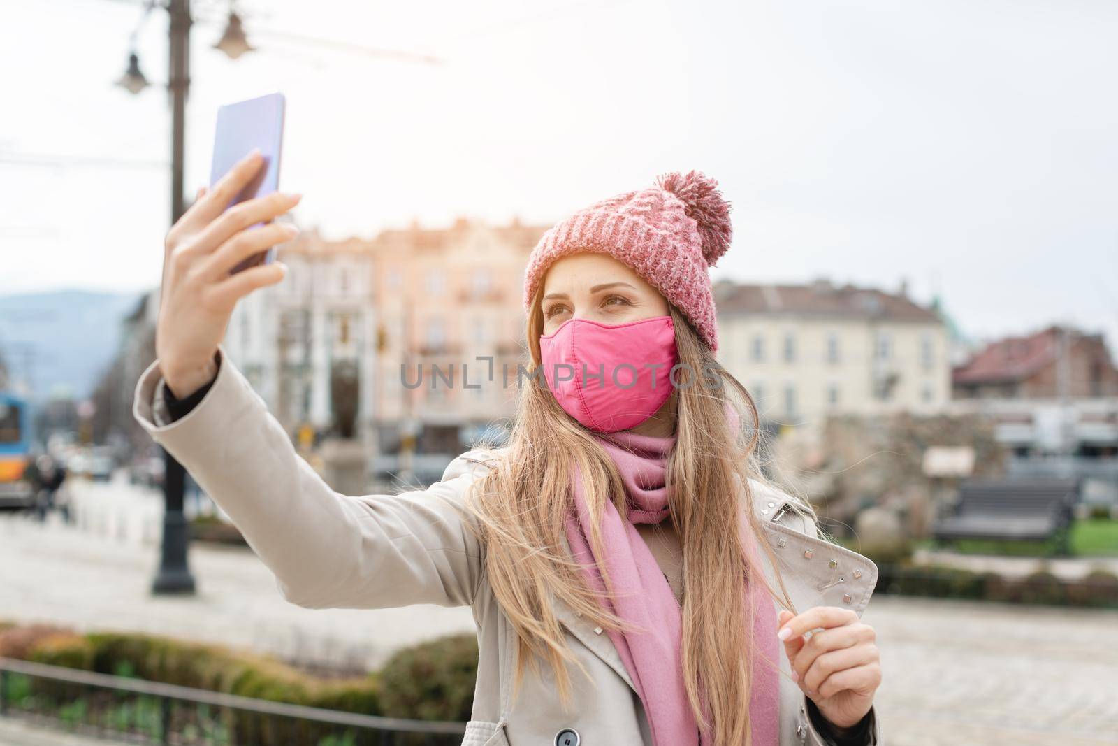 Woman wearing corona mask making selfie with phone in city