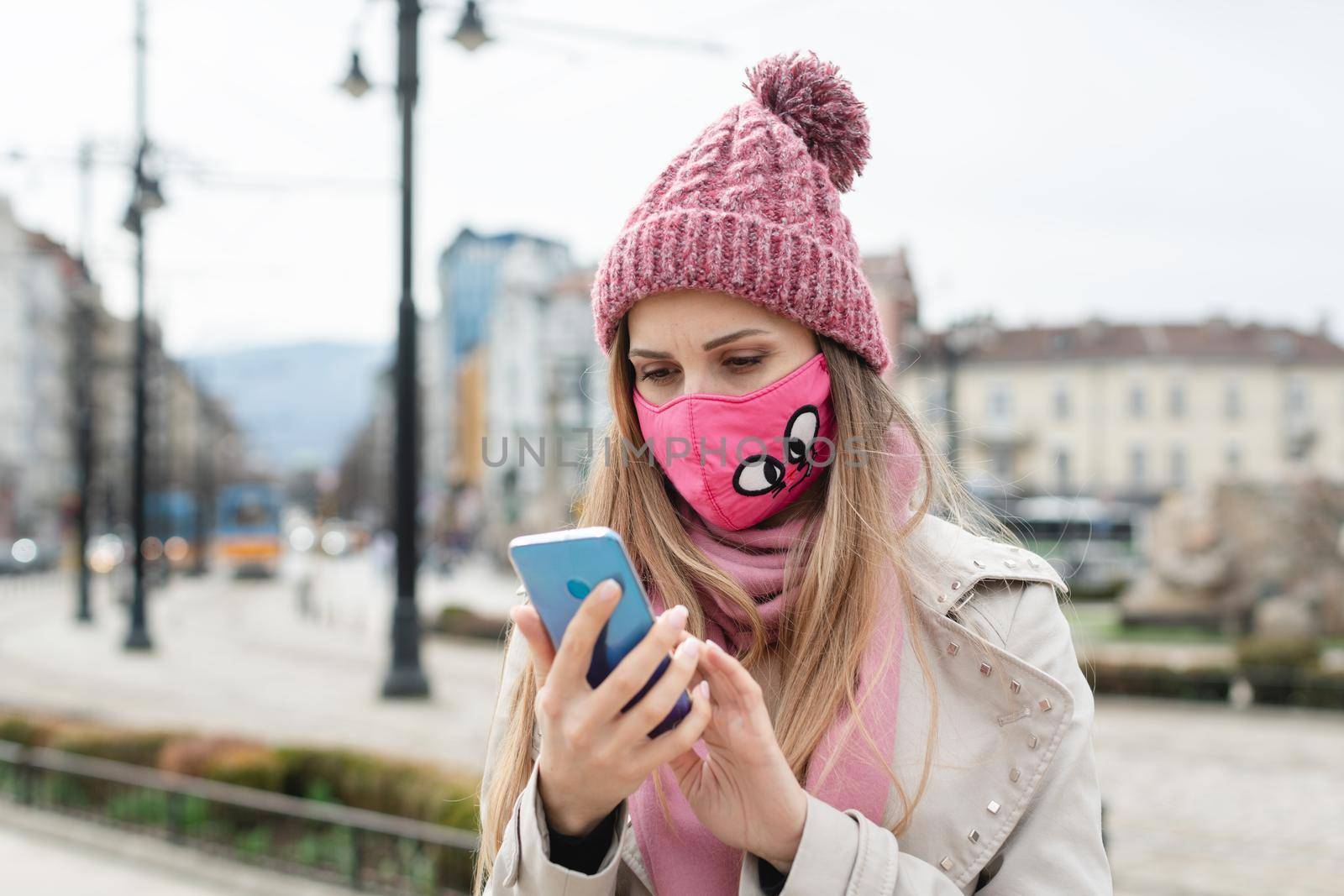 Anxious woman wearing corona mask checking news on her phone in lockdown city