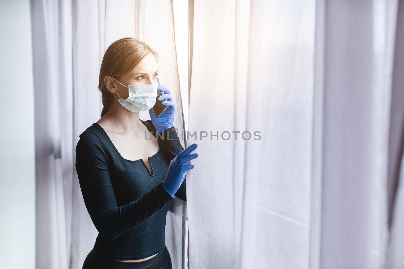 Woman in quarantine looking out of window using phone to call help for anxiety and depression