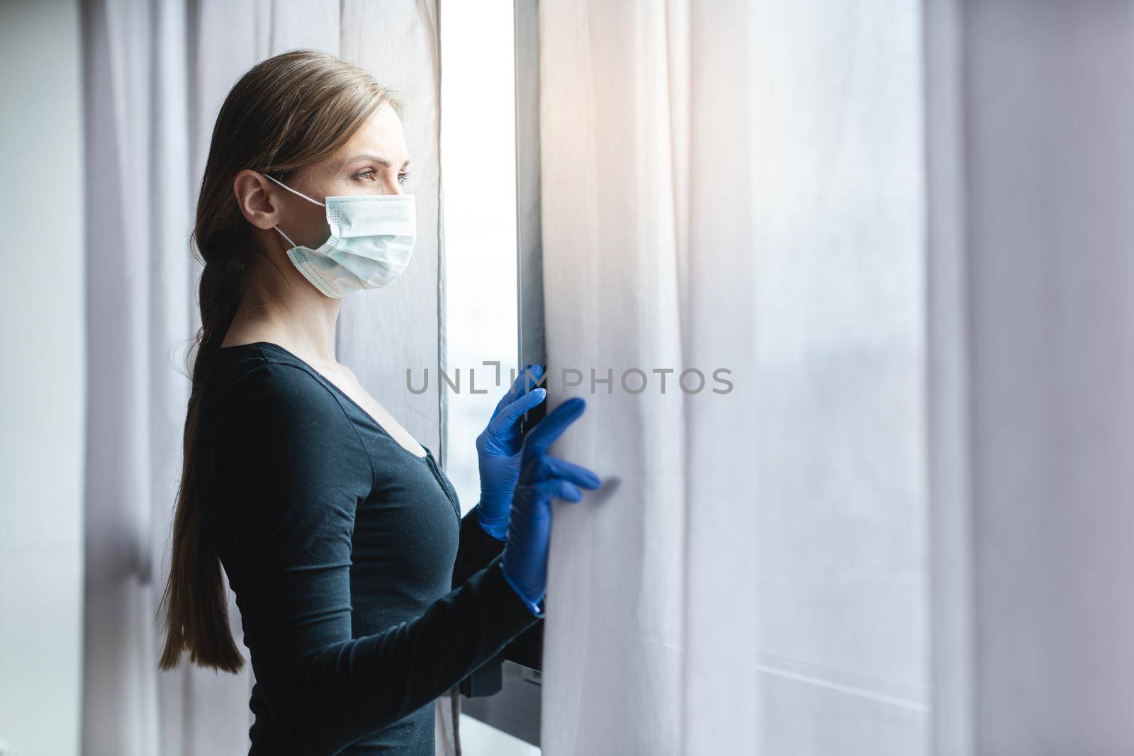 Bored woman in corona quarantine looking out of window to the street