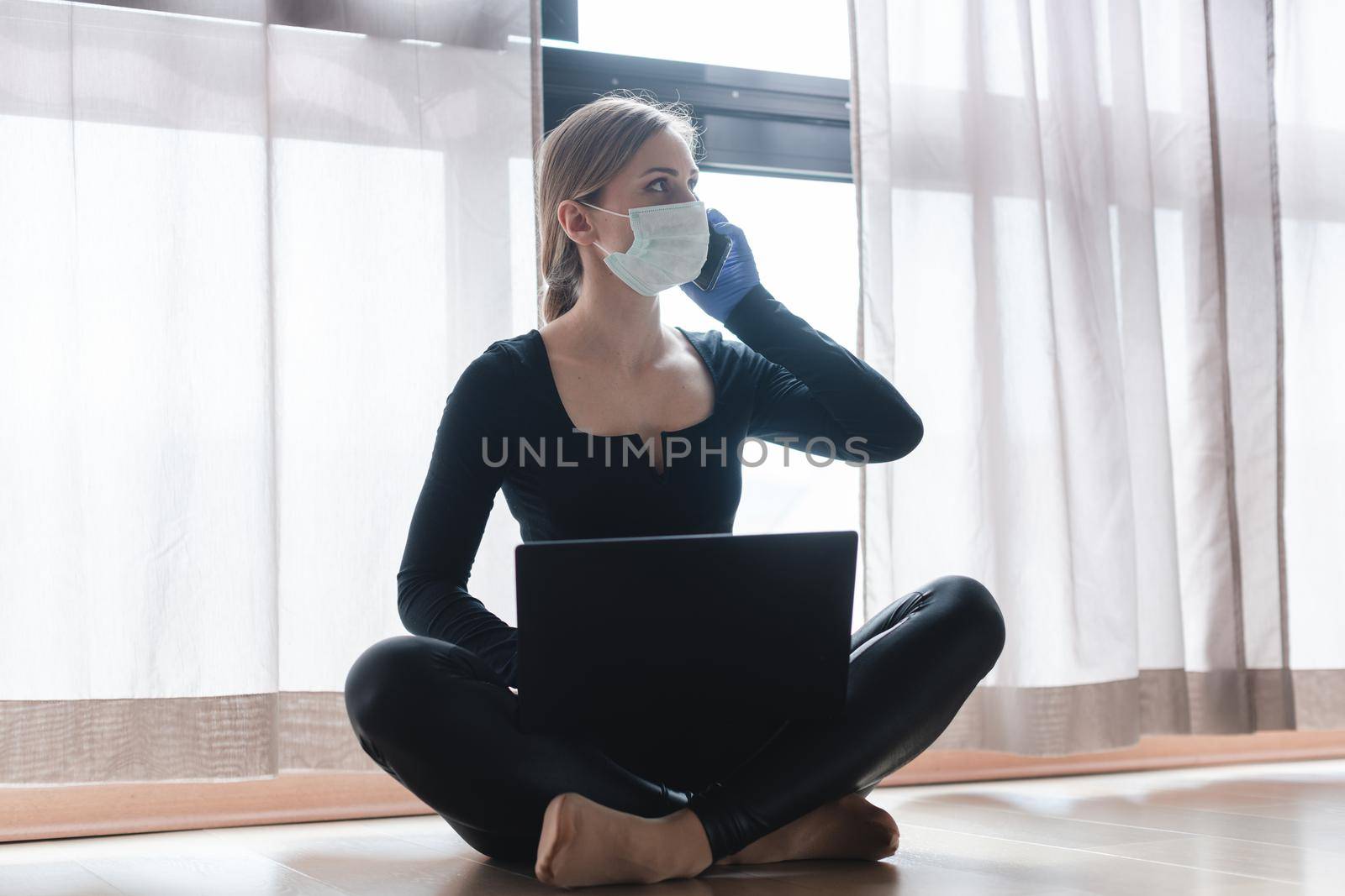 Woman in corona quarantine with phone and laptop by Kzenon