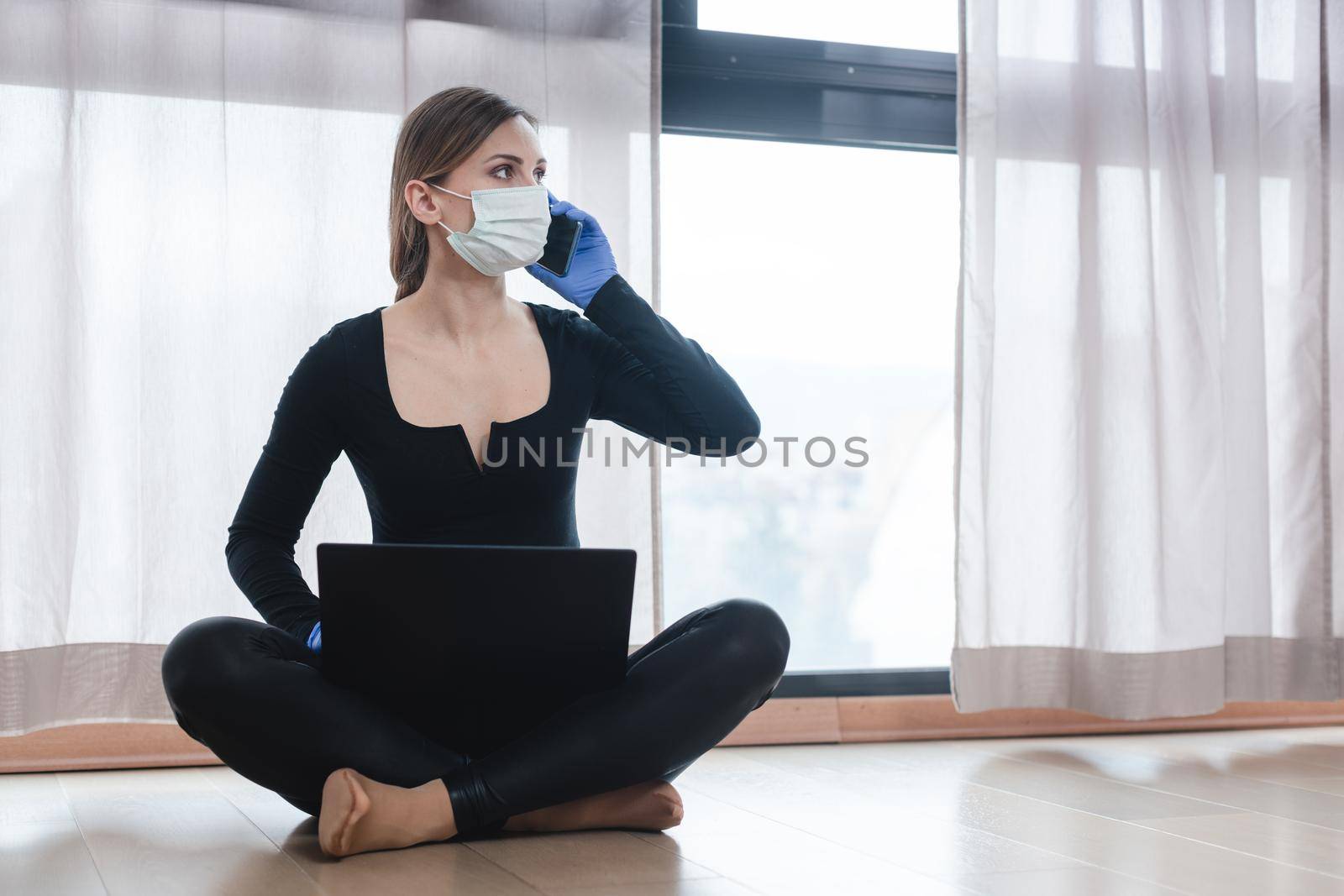 Woman in corona quarantine with phone and laptop by Kzenon