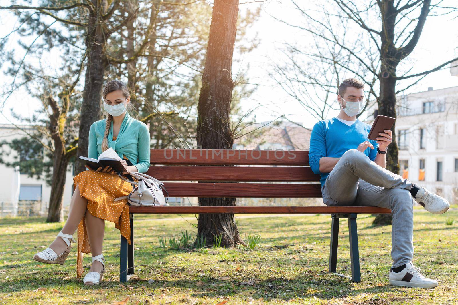 Woman and man in social distancing sitting on bench in park