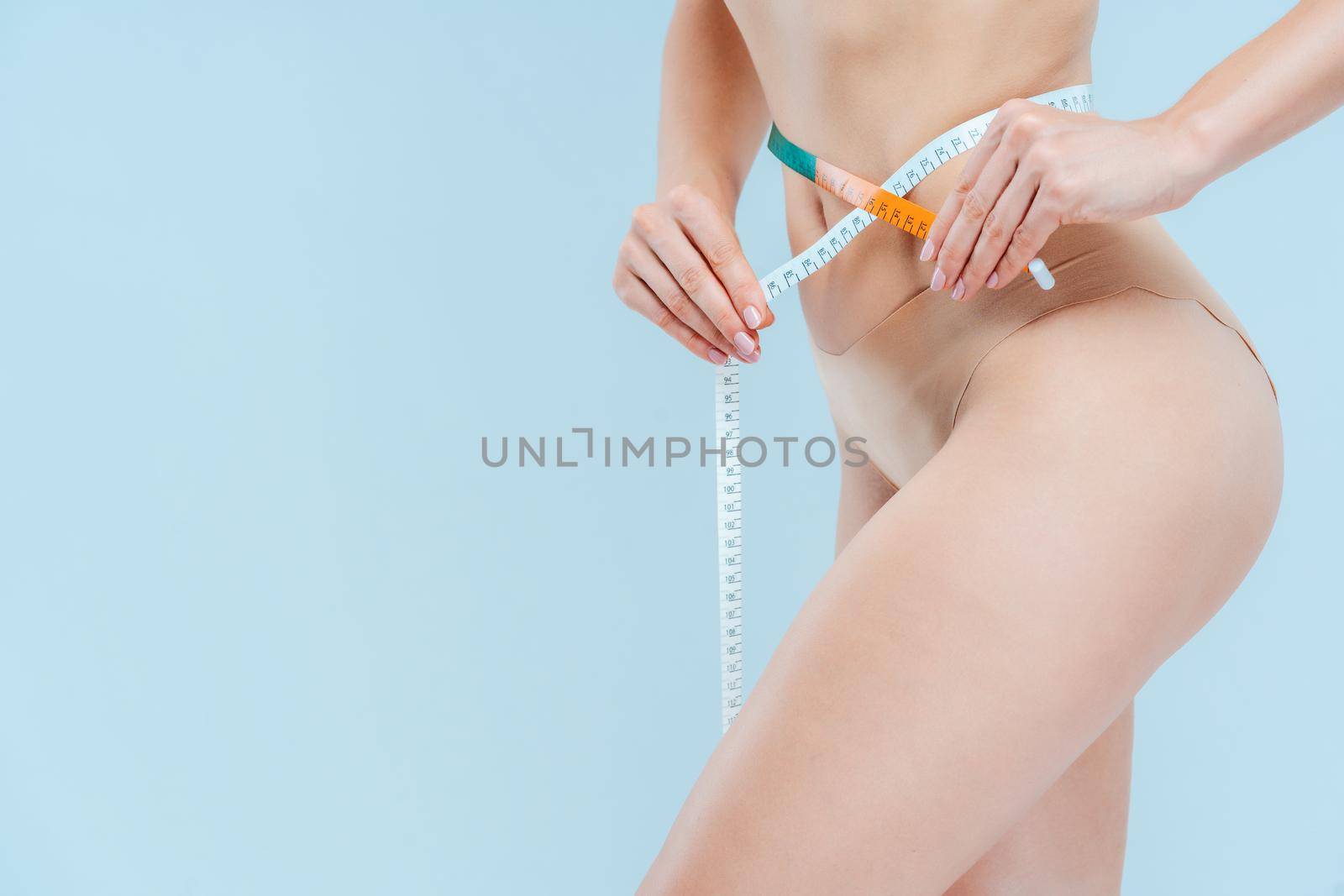 Very slim woman measuring her waist with tape measure, torso to be seen