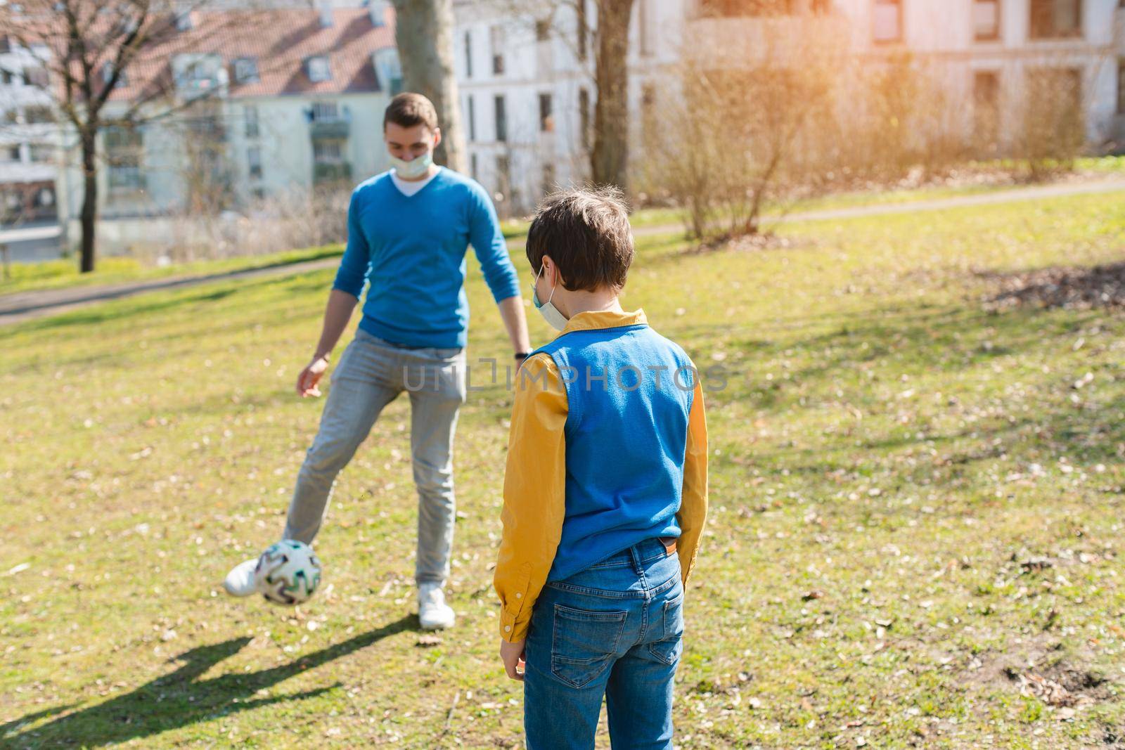 Dad and son playing soccer in park during coronavirus crisis by Kzenon