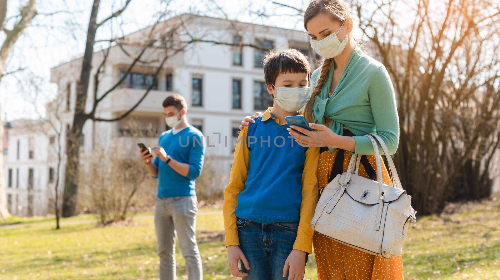 Family during corona crisis checking news on their phones standing in park