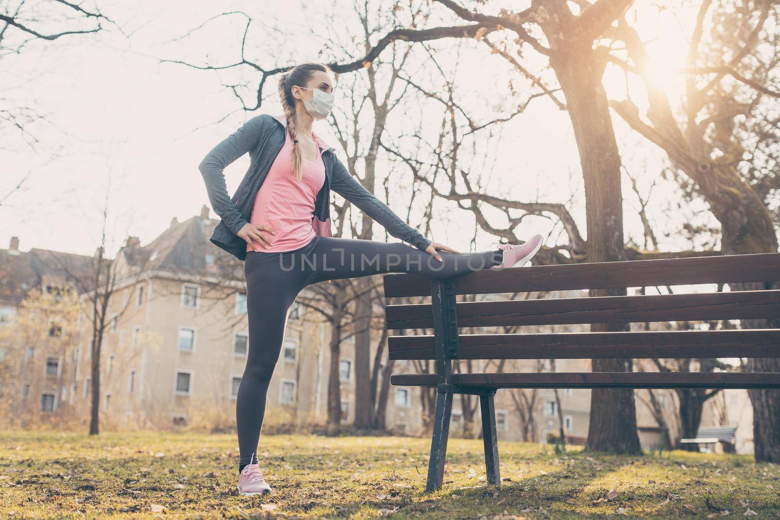 Woman wearing face mask stretching on a bench outdoors by Kzenon