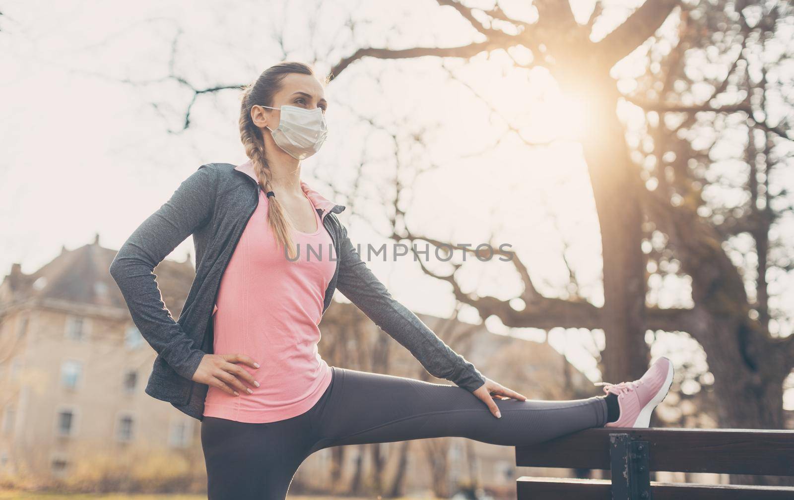 Woman wearing face mask stretching on a park bench outdoors