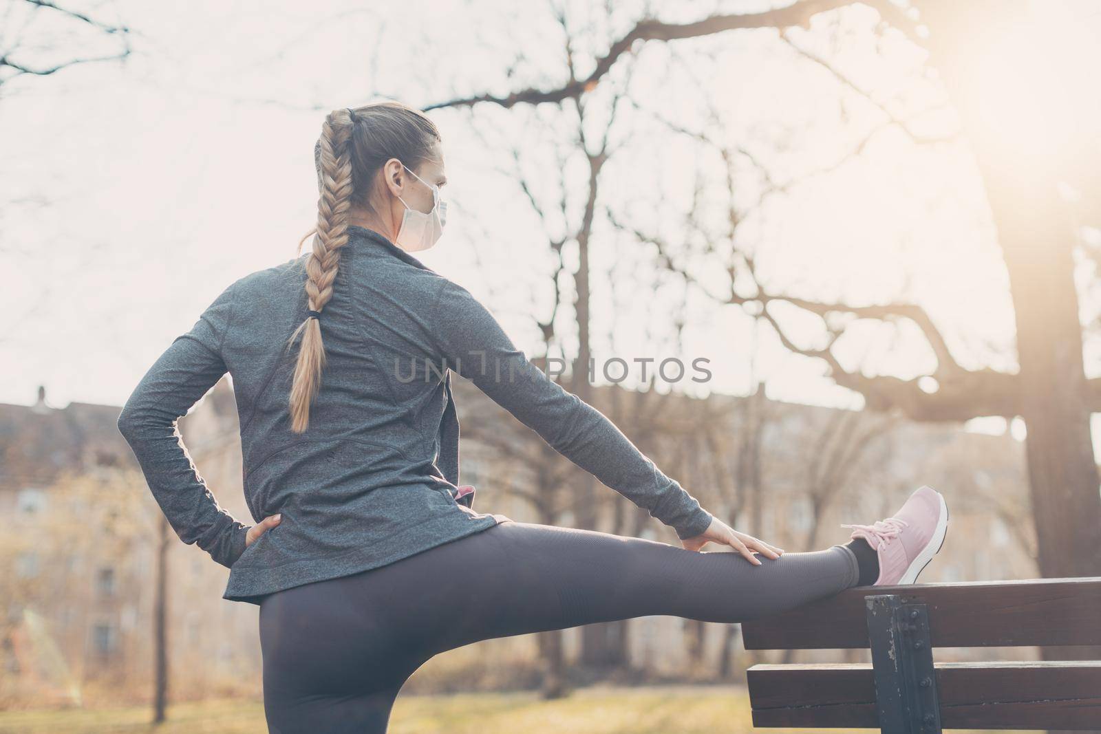 Woman wearing face mask stretching on a park bench outdoors