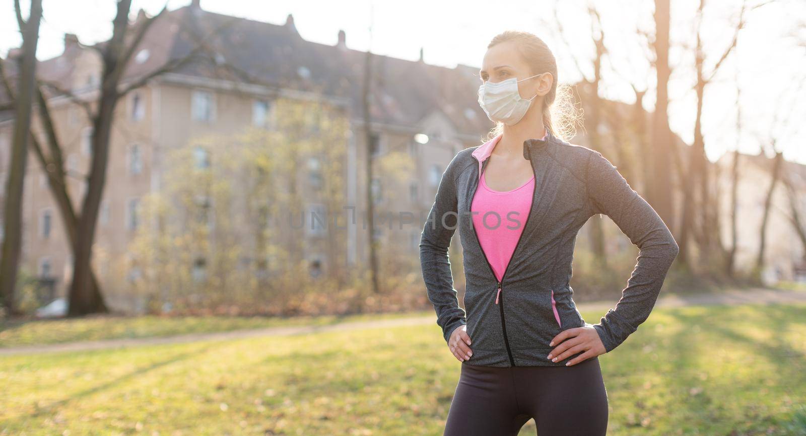 Fit woman during health crisis exercising outdoors wearing mask by Kzenon