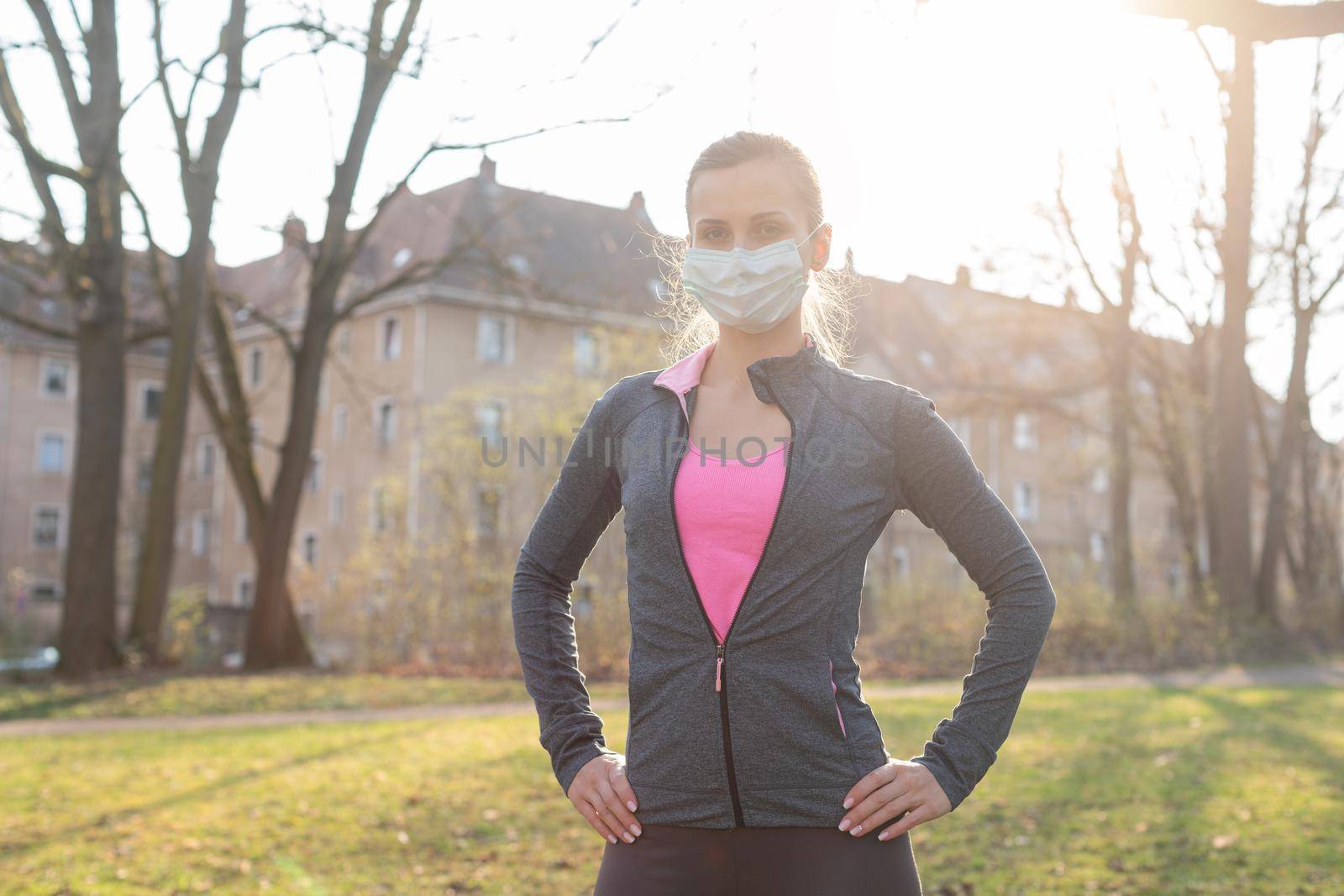 Fit woman during health crisis exercising outdoors wearing mask by Kzenon