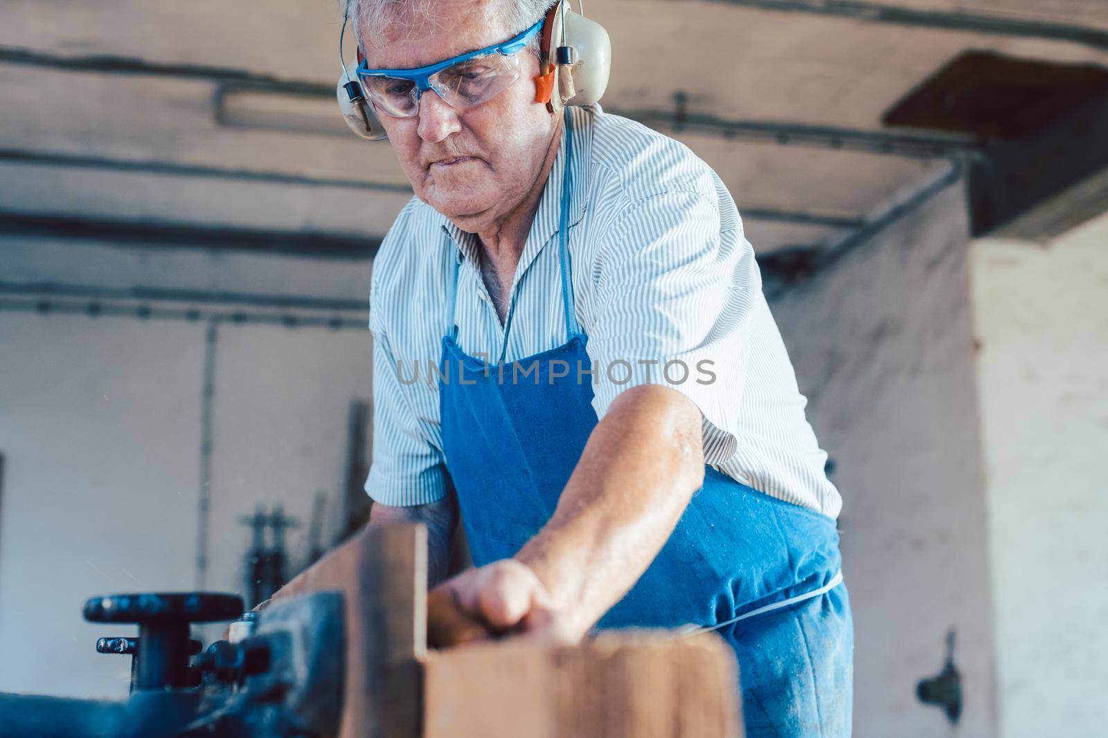 Senior carpenter with full protective workwear working with wood planer on workpiece