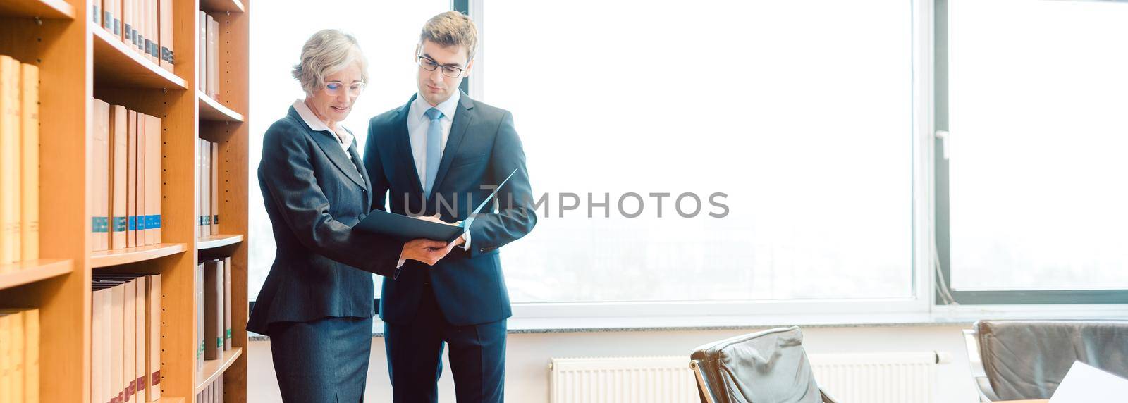 Senior and junior lawyer in law firm discussing strategy in a case reading the file