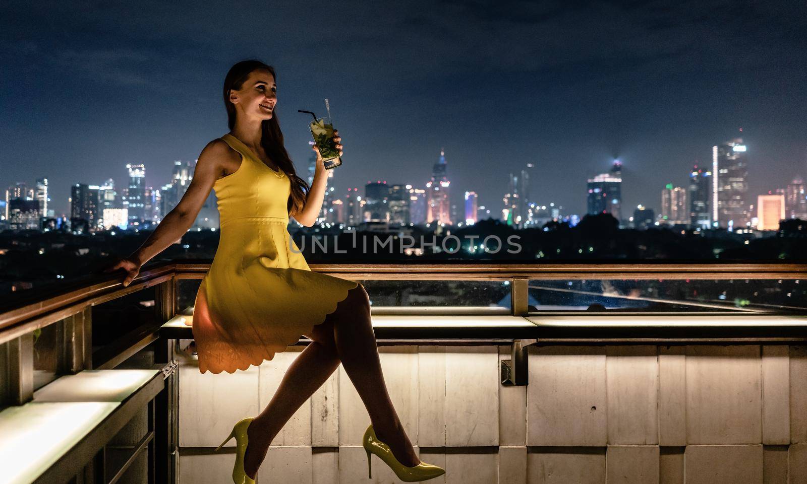 Woman having a drink on roof terrace overlooking the city skyline