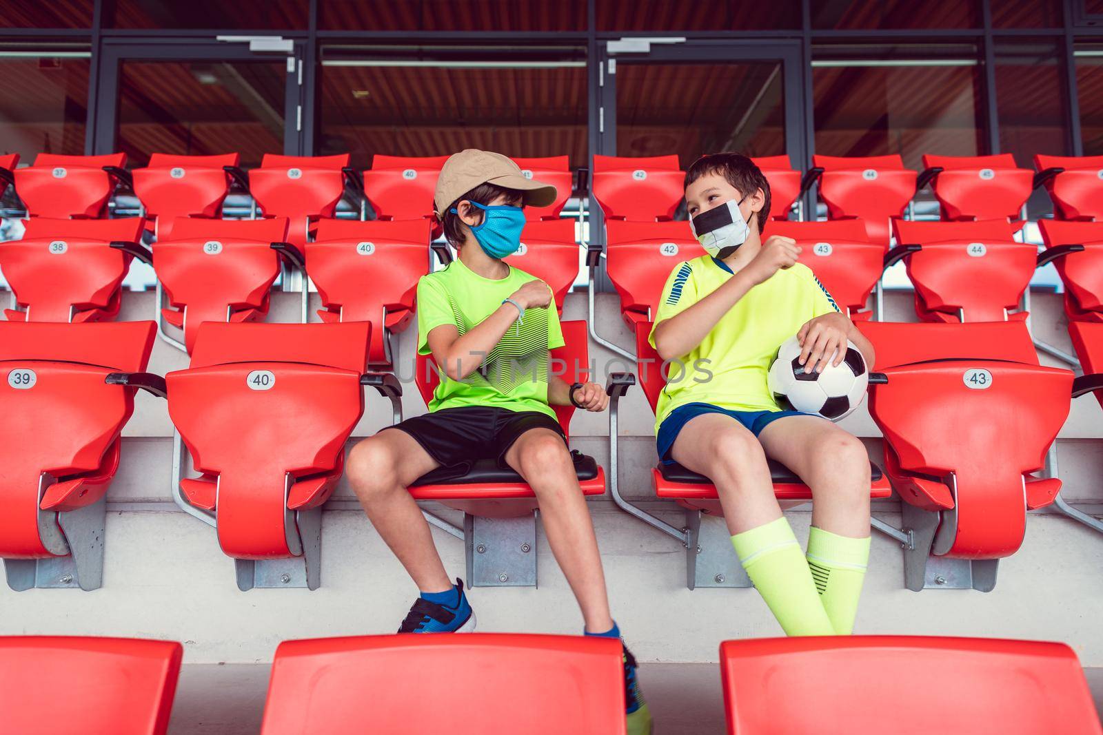 Two boys in a soccer stadium watching the game during covid-19 wearing face masks