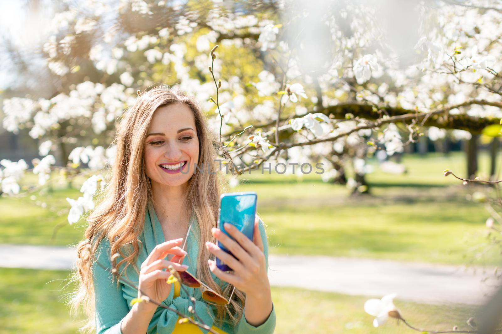 Young woman using her phone on a beautiful day in spring standing amid blossoming tree