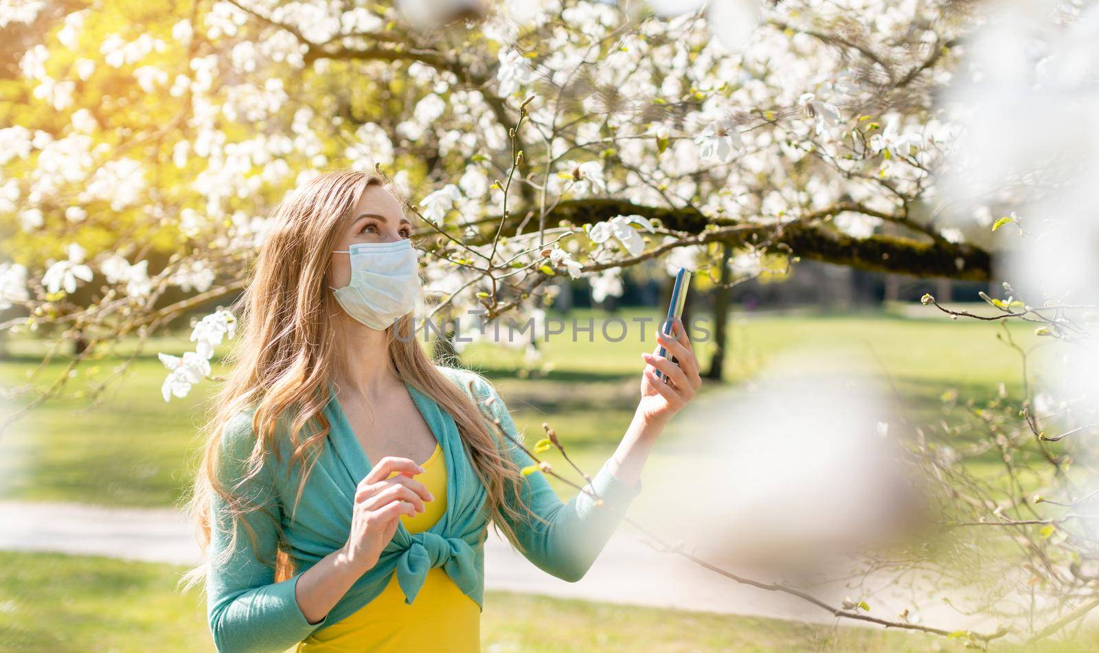 Woman enjoying the spring blossom despite the Coronavirus crisis taking picture with her phone
