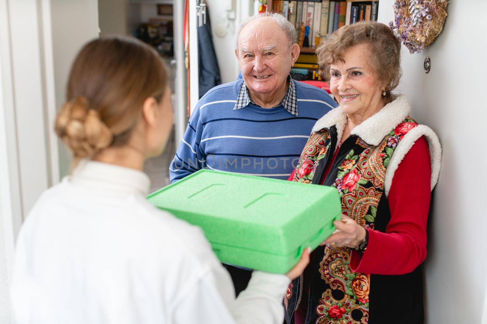 Senior couple greeting volunteer woman delivering a hot meal to their door